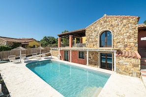 A poolside area with a stone building, a clear blue pool, and a fenced patio with lounge chairs. - Villa 'Pretziosa' with Private Pool, Wi-Fi and Air Conditioning (Castiadas)