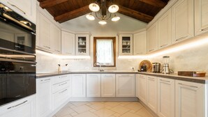 A kitchen with white cabinets, a black oven, a window with curtains, and a wooden ceiling. - Villa 'Pretziosa' with Private Pool, Wi-Fi and Air Conditioning (Castiadas)