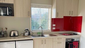 A modern kitchen with light wood cabinets, a stainless steel sink, a red backsplash, and a built-in oven.