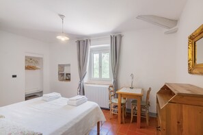 Une chambre à coucher avec un lit, un bureau en bois, une chaise, un miroir et une fenêtre avec des rideaux.