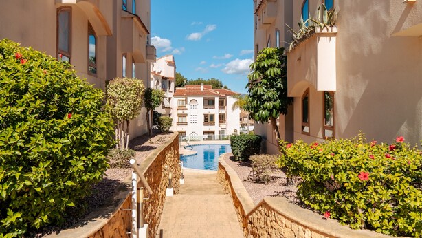 A pathway leading to a pool surrounded by greenery and buildings with balconies. - Apartment 'Tu Descanso' with Shared Pool, Wi-Fi and Air Conditioning (Alfaz del Pi)