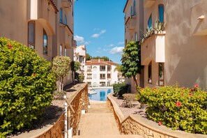 A pathway leading to a pool surrounded by greenery and buildings with balconies. - Apartment 'Tu Descanso' with Shared Pool, Wi-Fi and Air Conditioning (Alfaz del Pi)