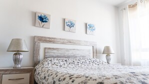 A bedroom with a wooden headboard, two bedside lamps, a floral bedspread, and three wall-mounted paintings. - Apartment 'Tu Descanso' with Shared Pool, Wi-Fi and Air Conditioning (Alfaz del Pi)