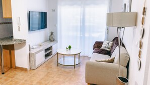 A modern living room with a sofa, a coffee table, a flat-screen TV, and a lamp. - Apartment 'Tu Descanso' with Shared Pool, Wi-Fi and Air Conditioning (Alfaz del Pi)