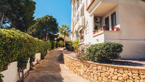A pathway leading to a building with a stone retaining wall, potted plants, and a clear blue sky. - Apartment 'Tu Descanso' with Shared Pool, Wi-Fi and Air Conditioning (Alfaz del Pi)