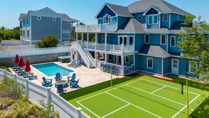 Een tweelaags huis met een zwembad, terras en een tennisbaan.