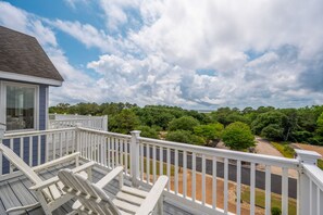 A wooden deck with white railings overlooking a road and dense greenery.