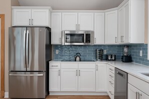 A modern kitchen with white cabinets, stainless steel appliances, a blue-tiled backsplash, and a wooden floor.