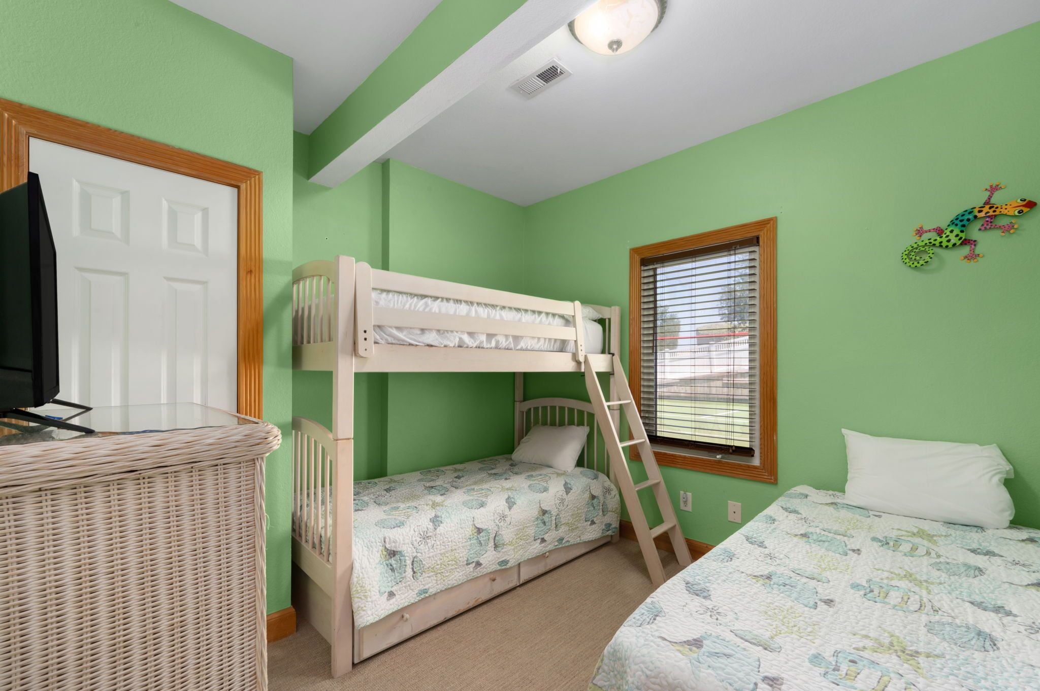 A bunk bed room with a television on a stand, a window with blinds, and a wall decoration.