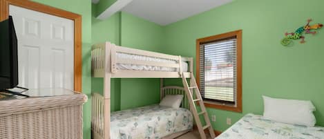 A bunk bed room with a television on a stand, a window with blinds, and a wall decoration.