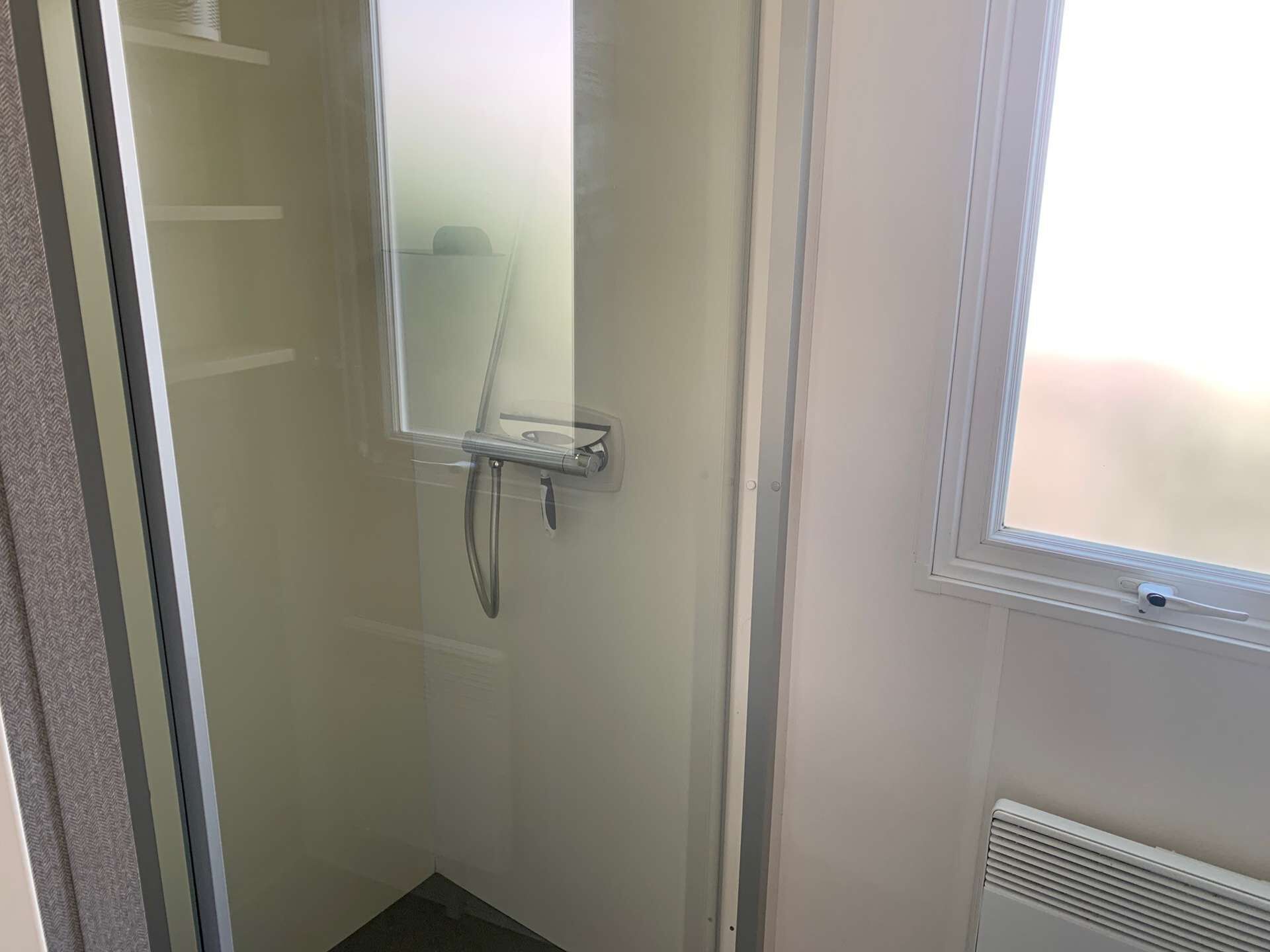 Un espacio de ducha pequeño y cerrado con puerta de vidrio, un perchero y una ventana.