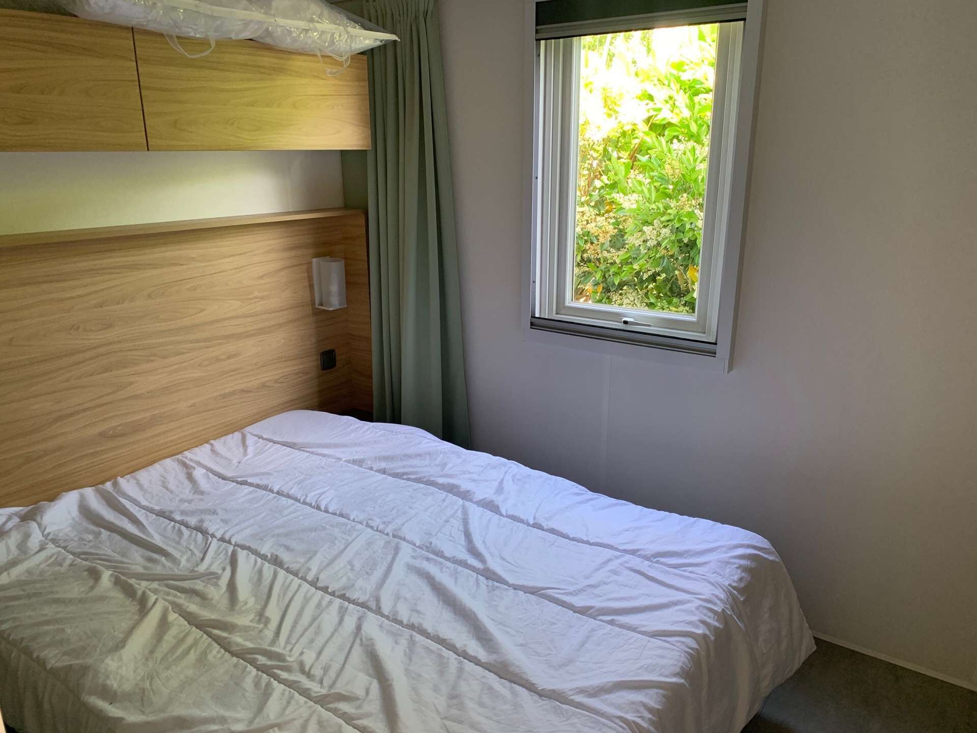 Un dormitorio con cabecera de madera, ventana con vistas a la vegetación y cama blanca.