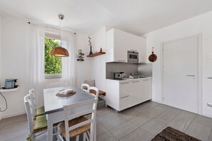 Moderni keittiö, jossa on valkoiset kaapit, ruokapöytä tuoleineen ja riippuvalaisin.