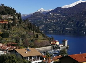 Un pueblo a orillas de un lago con una torre destacada, barcos amarrados a la orilla y montañas al fondo.