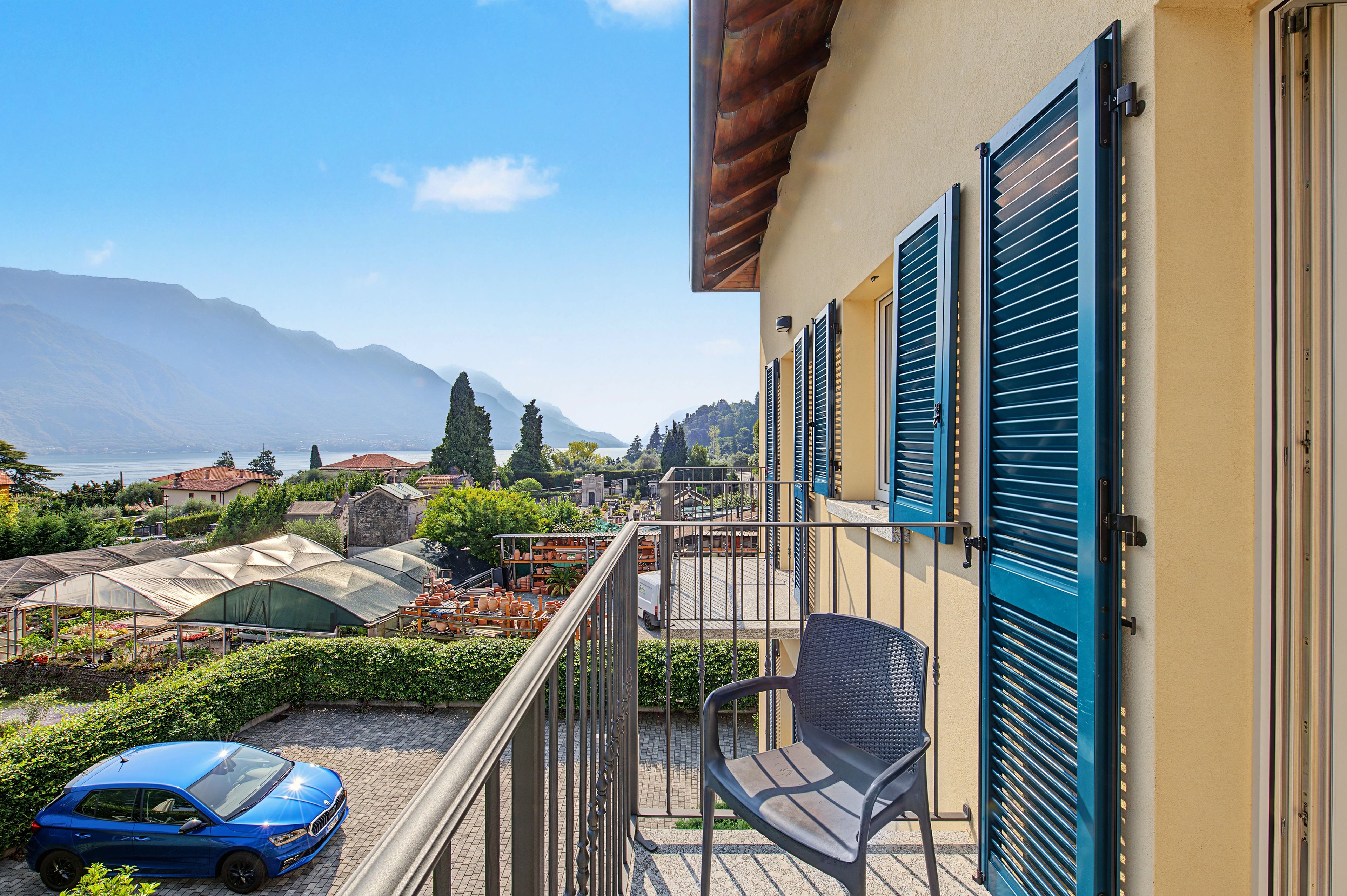 Ein Balkon mit Blick auf einen Garten, ein blaues Auto und ein Berg im Hintergrund.