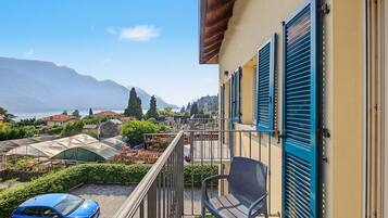 Ein Balkon mit Blick auf einen Garten, ein blaues Auto und ein Berg im Hintergrund.