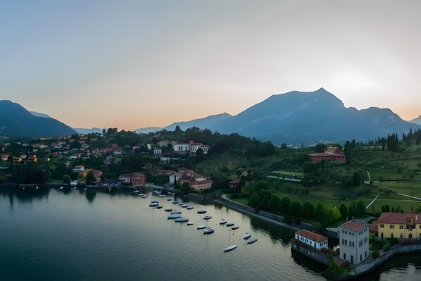 Un pueblo a orillas de un lago, con barcos, edificios y montañas al fondo.
