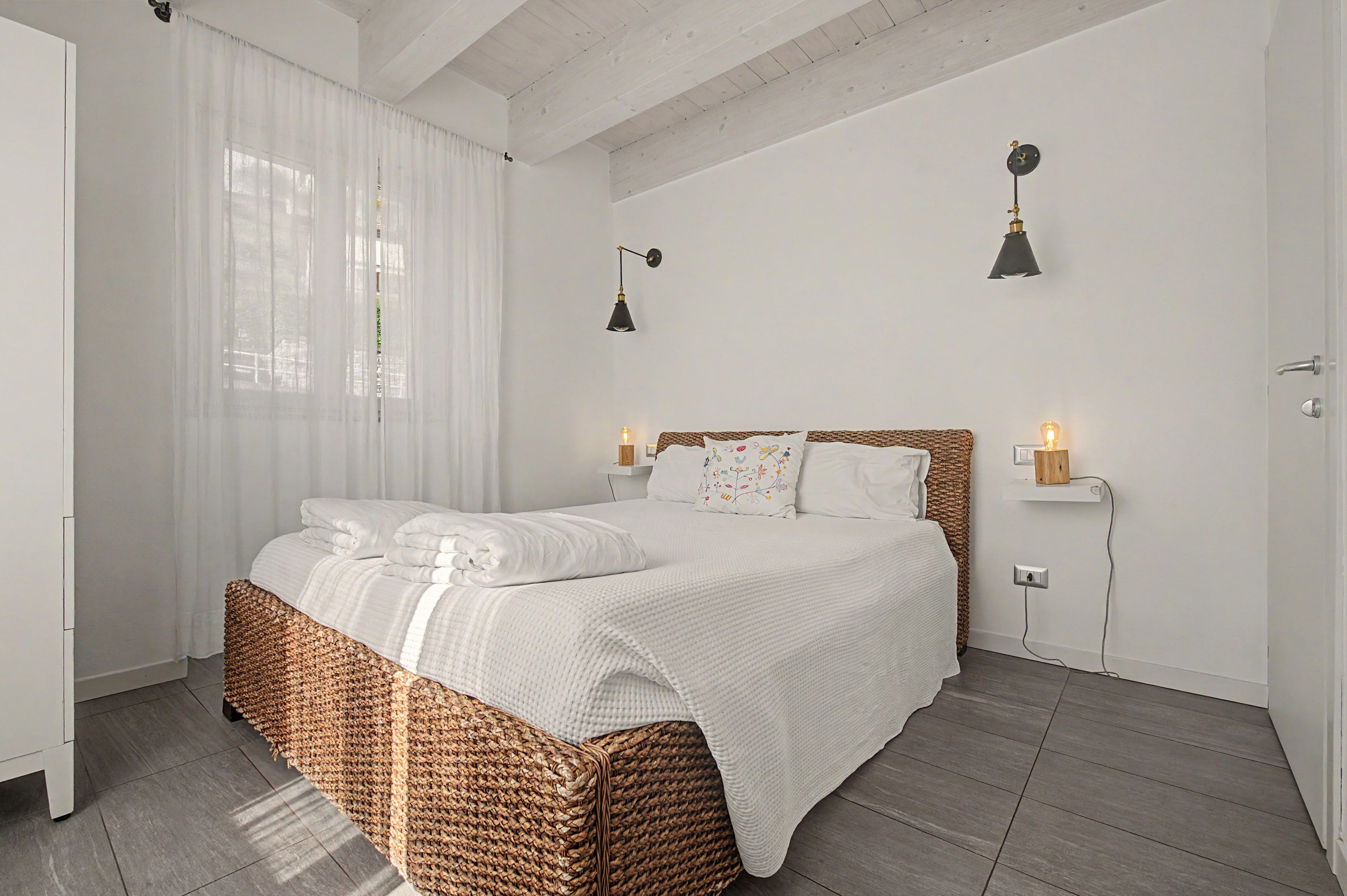 Ein Schlafzimmer mit einem Bett, weißen Vorhängen, einer Holzbalkendecke und zwei Wandleuchten.
