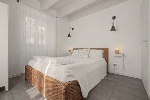 Un dormitorio con una cama, cortinas blancas, techo de madera y dos lámparas fijadas a la pared.
