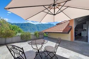 A patio with a table and chairs, a large umbrella, and a view of mountains. - Apartment 'Brezza' with Lake View, Wi-Fi and Air Conditioning (Bellagio)