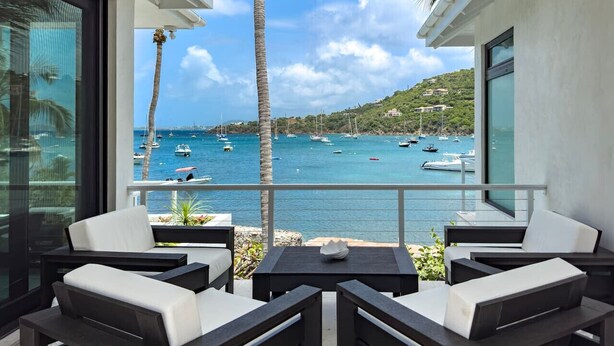 Ein Balkon mit Sitzgelegenheit, Blick auf Boote auf blauem Wasser und eine Hügelkulisse im Hintergrund.