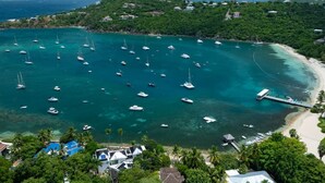 Eine Küstenlandschaft mit zahlreichen Booten, die in klarem, türkisblauem Wasser vor Anker liegen, einer in das Meer führenden Mole und üppiger, umliegender Vegetation.