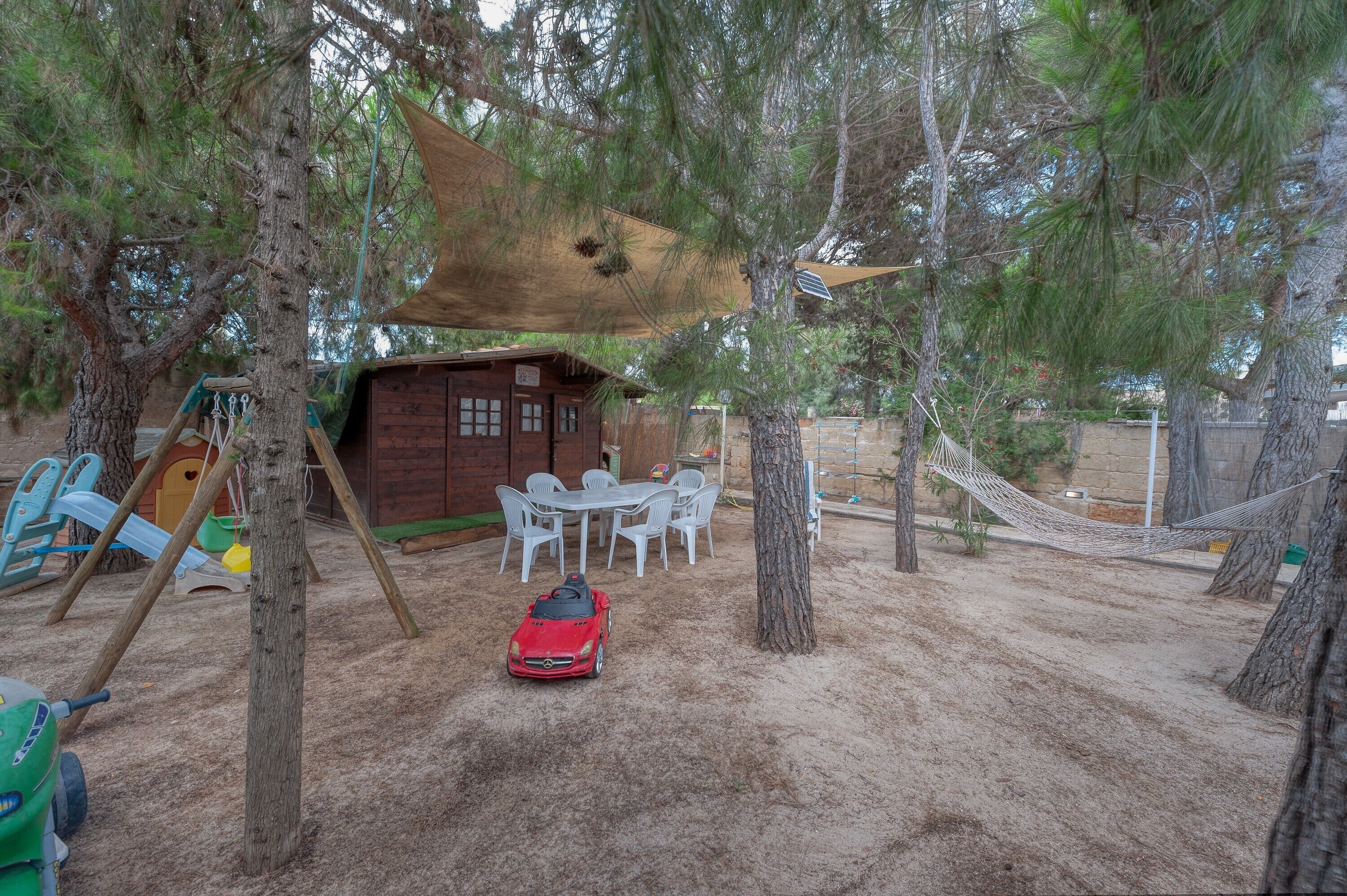 Eine Holzhütte mit Spielbereich, darunter eine Schaukel und ein Tisch mit Stühlen.
