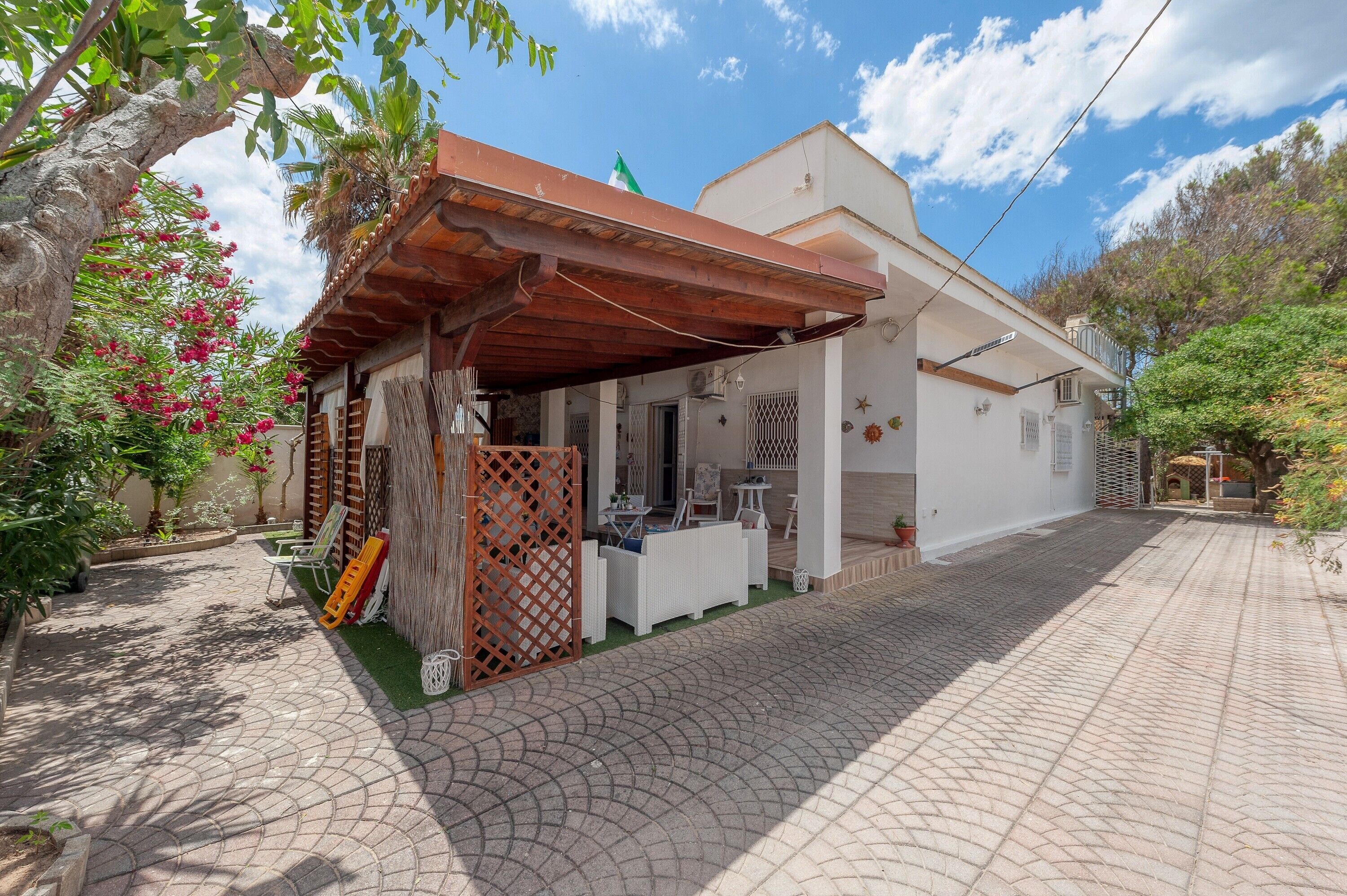 Un bâtiment blanc doté d’un patio couvert, d’un petit espace extérieur aménagé avec des sièges et d’un chemin pavé.