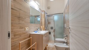 Moderni kylpyhuone, jossa on puinen allaskaappi, lasinen suihkuseinä ja wc.