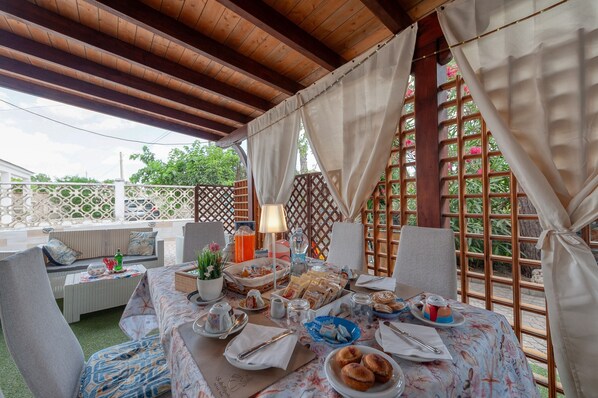An outdoor dining area with a table set for a meal, surrounded by wooden lattice walls and covered with white curtains.