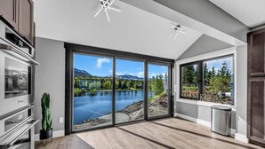 A modern kitchen with a large sliding glass door leading to a scenic outdoor view of a lake and mountains. - Mountain Lake Sanctuary in Alaska Up to 22 Guests (Anchorage)