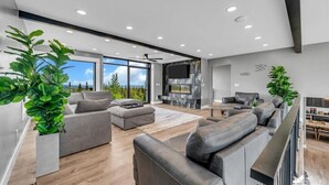 A modern living room with a fireplace, grey sofas, and large windows offering a view of the outdoors. - Mountain Lake Sanctuary in Alaska Up to 22 Guests (Anchorage)