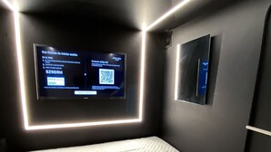 A modern room with a large flat-screen TV mounted on the wall, a small secondary screen, and a quilted mattress. - Habitación  Tipo Cápsula (Bogota)