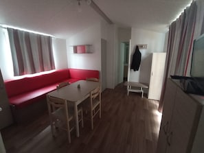 Une pièce avec un canapé rouge, une petite table et des chaises. On y trouve également un porte-manteau et un meuble.