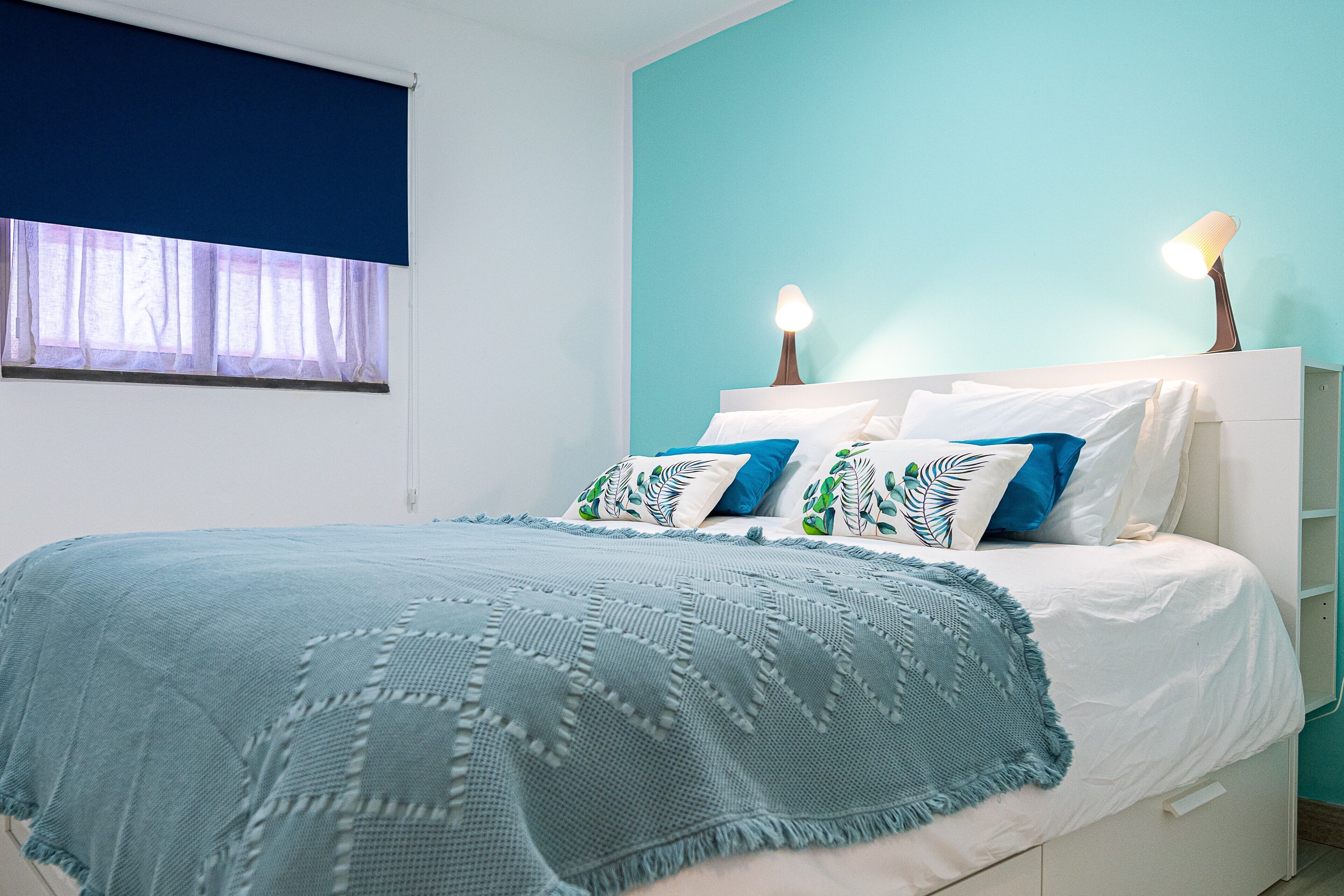 A bed with a blue blanket, white pillows, and a bedside lamp.