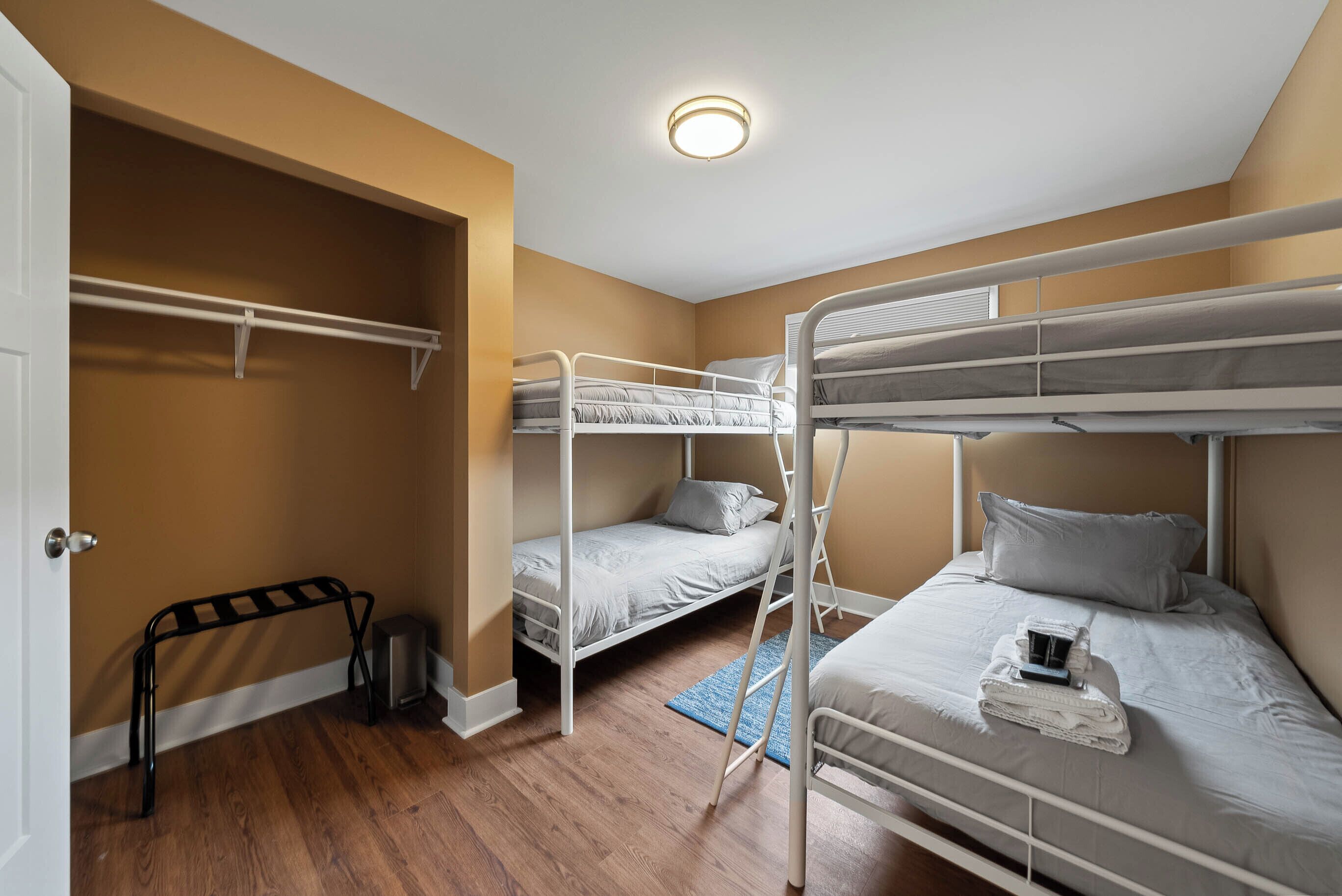 A bunk bed room with a metal ladder, a small closet, and a blue rug.