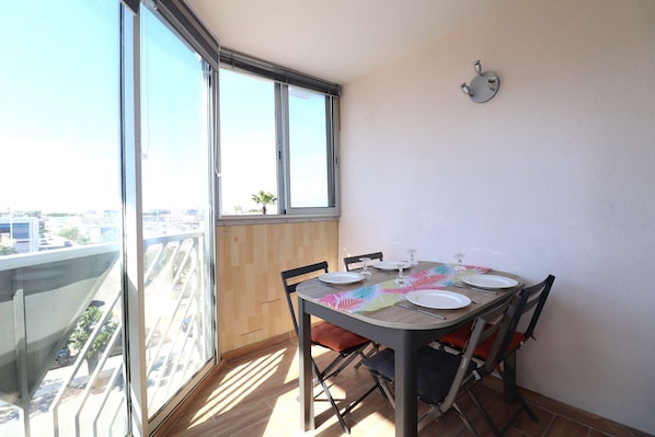 A dining area with a table set for four, a window with blinds, and a view of a cityscape.