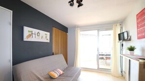 A room with a sofa, a television, a small table, and a window with curtains.