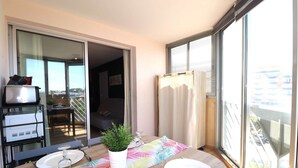 A balcony with a dining table set for two, a potted plant, and a view of the cityscape.