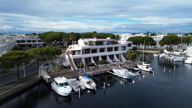 A marina with boats docked, a modern building with multiple levels, and a clear sky.