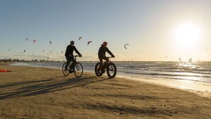 A beach with two cyclists and multiple kites in the background.