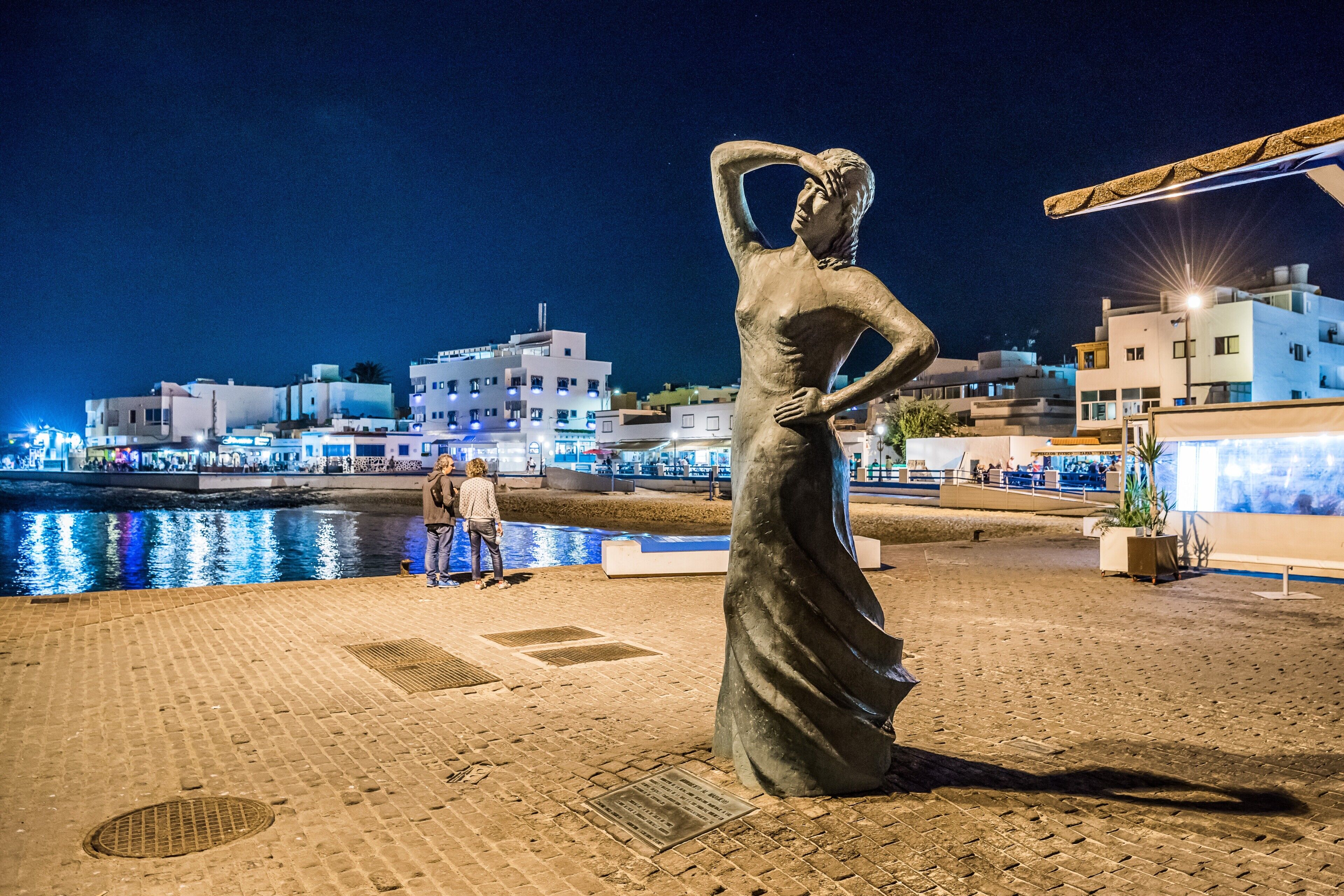 A nighttime view of a cityscape with a prominent statue in the foreground.