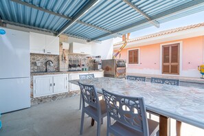 Un espace cuisine extérieur abrité, comprenant une table et des chaises, un réfrigérateur et une cuisinière.