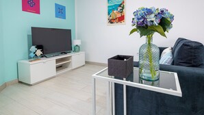 A modern living room with a flat-screen TV, a glass coffee table, a dark-colored sofa, and a vase with flowers.