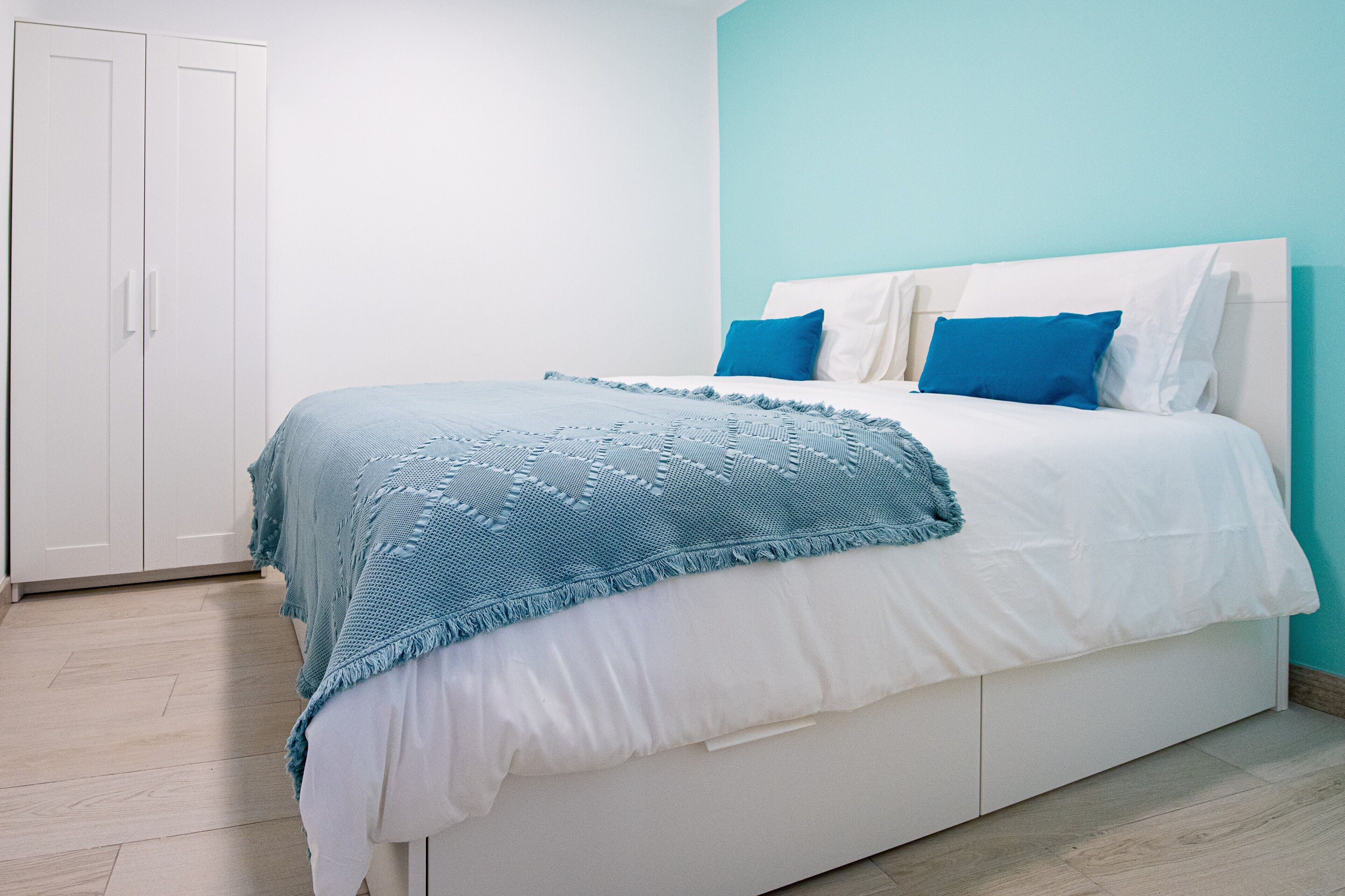 Een slaapkamer met een bed, een witte kledingkast en lichtblauwe wanden.