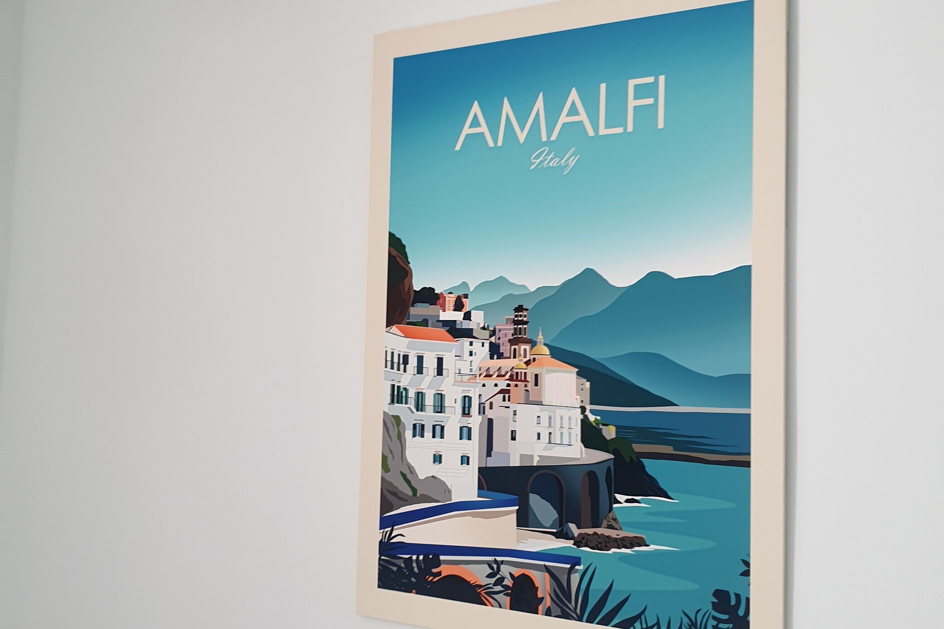 Een lijstwerk met een afbeelding van Amalfi, Italië, dat een kustplaats toont met gebouwen en bergen.