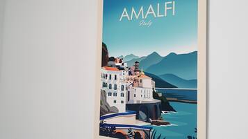 Una obra de arte enmarco muestra Amalfi, Italia, con un pueblo costero, edificios y montañas.