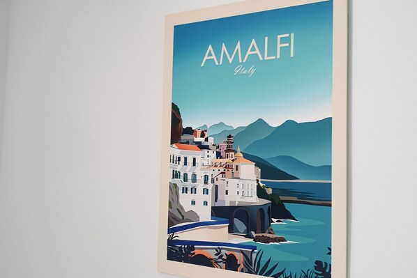 Une œuvre d'art encadrée représentant Amalfi, en Italie, avec une ville côtière, des bâtiments et des montagnes.