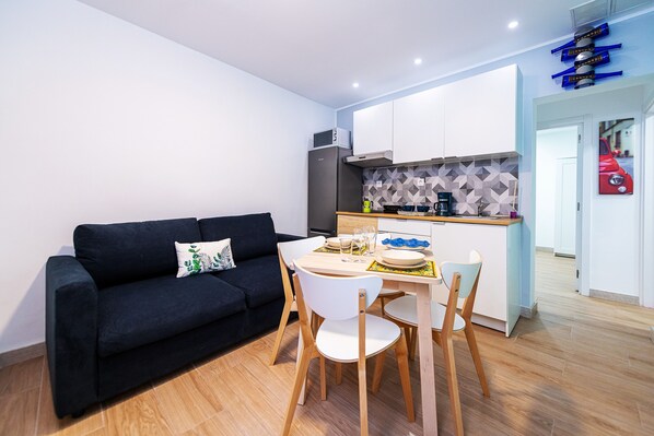 A modern kitchen with white cabinets, a black sofa, and a dining table with chairs.