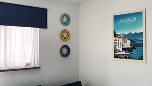 A room with a window, a wall-mounted artwork of Amalfi, Italy, and three decorative plates. - Vacation 'Amalfi' with Wi-Fi (Corralejo)